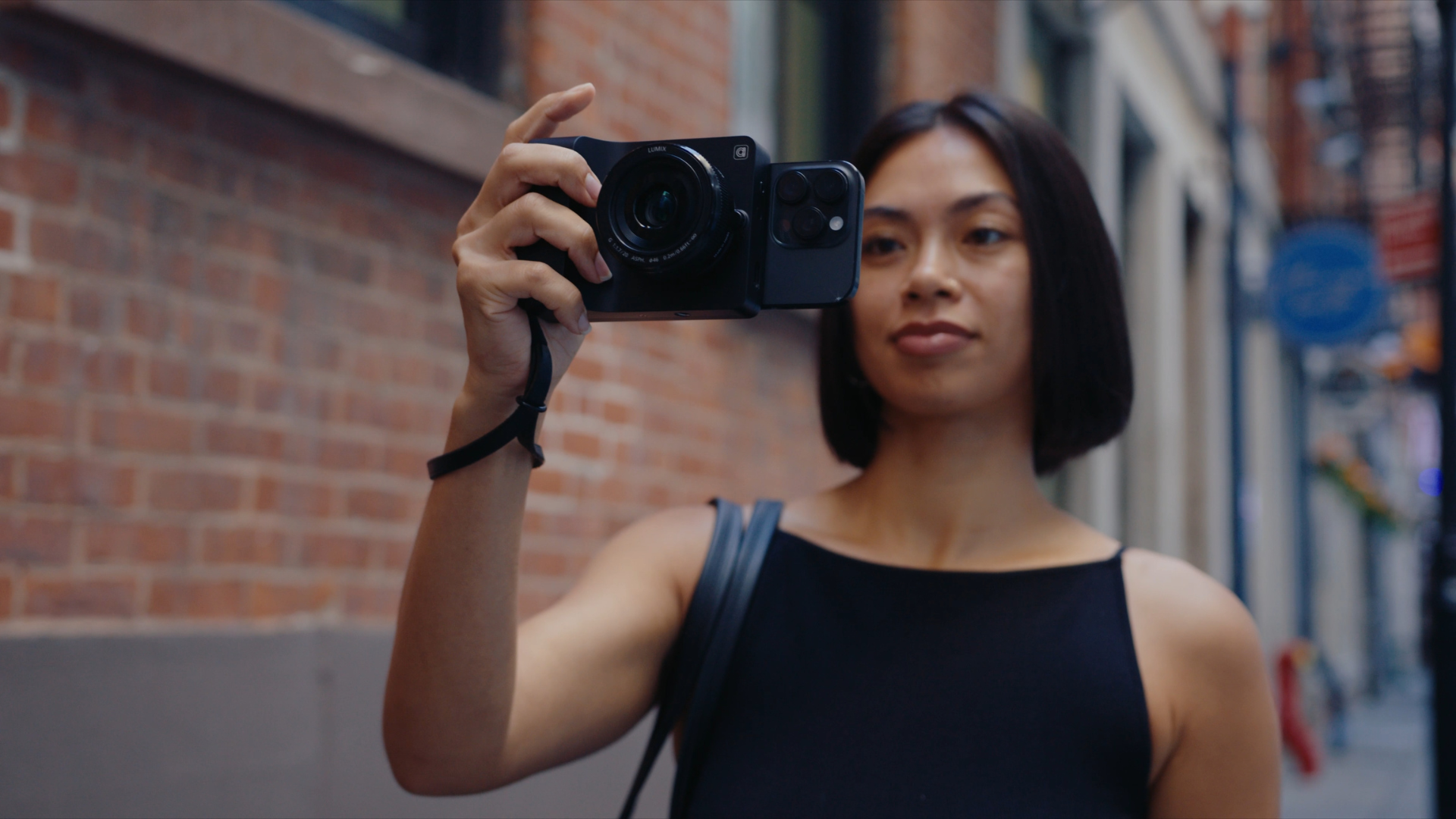 A photograph of a woman in a white t-shirt holding Camera Intelligence's 'Caira' product with a wide-angle lens. She is looking at the back of the camera as if focusing on the photo or videography.
